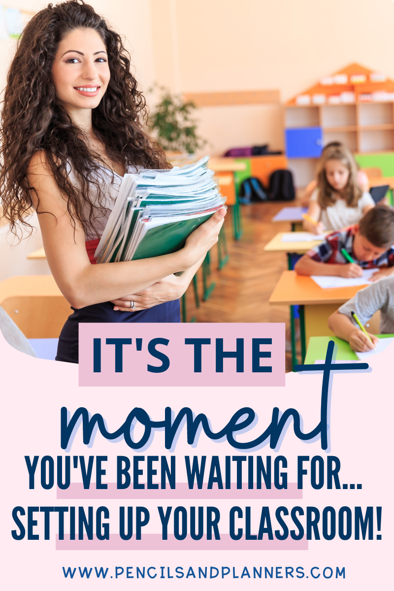 teacher holding a pile of books and papers smiling at the camera, students writing and working behind her, text overlay says it's the moment you've been waiting for... setting up your classroom